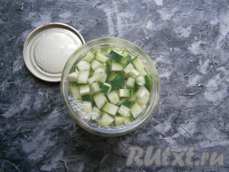 Полностью залить кубики огурчиков в банках кипящей водой. Баночки, прикрыв заранее прокипячёнными крышками, оставить минут на 15. Далее воду из банок вылить в раковину, снова залить кубики огурчиков кипящей водой и оставить на 10 минут.