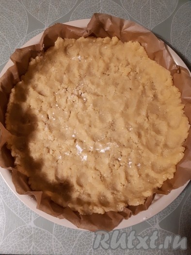 Форму для выпечки застелить пергаментной бумагой. В форму натереть на тёрке охлаждённое тесто. Равномерно распределить по всей поверхности формы, примять пальчиками, формируя бортики.
