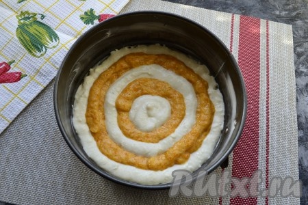 Дно разъёмной формы диаметром 18 см застелить пергаментом. Затем всю форму тщательно смазать сливочным маслом. Выдавливать по кругу кольцами поочередно, начиная от края формы, творожную и тыквенную смеси, как на фото.
