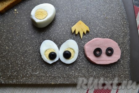 От варёного яйца острым ножом отрезать вертикально две части с правой и левой стороны яйца (для глаз), из кружка колбасы вырезать овал (нос) и из ломтика сыра вырезать чубчик для бычка. Одну оливку нарезать кружочками и выложить в качестве ноздрей на нос из колбасы, вторую оливку разрезать пополам и выложить в качестве зрачков на яйца (см. фото).