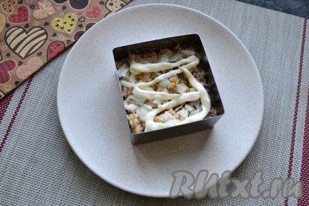 Поверх рыбы равномерно распределить очищенный и тонко нарезанный лук, смазать майонезом.