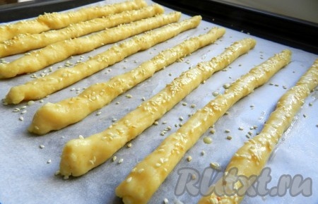 Противень застелить бумагой для выпечки. Тесто разделить на равные части (я разделила на 10 частей). Из каждой части теста скатать палочку, как на фото, и выложить на застеленный противень. Небольшое яйцо взбить вилкой в небольшой ёмкости до однородности. Смазать яйцом каждую сырную палочку, посыпать кунжутом. Выпекать в разогретой до 200 градусов духовке 20-25 минут.