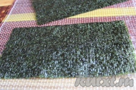 Коврик макису или салфетку-циновку нужно обязательно обернуть пищевой плёнкой, так будет намного удобнее. Стандартный лист нори разрезать на 2 половины и положить блестящей стороной на циновку.