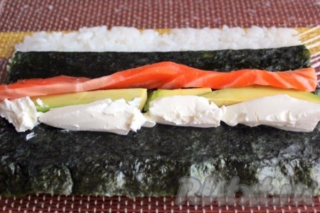 Перевернуть таким образом, чтобы рис оказался внизу, а нори наверху. И посередине выложить начинку.