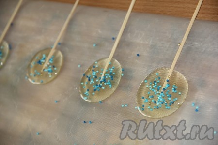 Снять сотейник с огня и подождать минуту (за это время пузыри осядут). На силиконовый (или тефлоновый) коврик налить чайную ложку сиропа. Сироп ровненько сформирует кружок. Сразу вставить палочку и, по желанию, посыпать цветной посыпкой. Аналогично сформировать все леденцы на палочках, используя весь сваренный сироп. Готовые леденцы оставить при комнатной температуре на 20 минут (до полного застывания).
