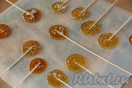 Когда готовила вторую партию леденцов, в самом конце варки я добавила каплю гелевого красителя (можно взять любой краситель), аккуратно перемешала, сняла с огня и аналогично сформировала леденцы, наливая сироп чайной ложкой на тефлоновый (или силиконовый) коврик и вставляя шпажки, посыпала цветной посыпкой.
