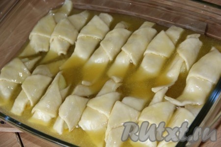 Выложить рогалики из слоёного теста с яблоками в жаропрочную форму, залить смесью масла и сахара.
