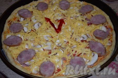 Посыпаем пиццу натёртым сыром. По кругу выкладываем 12 кружочков колбасы в форме циферблата. По центру пиццы кладём стрелки, указывая время без 5 минут двенадцать - как символ наступления Нового года.
