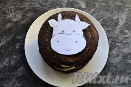 Сложить панкейки друг на друга, верхний панкейк смазывать кремом не нужно. На бумаге нарисовать и вырезать шаблон-картинку бычка, разместить её по середине верхнего панкейка.
