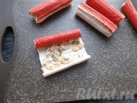 Размороженные крабовые палочки аккуратно развернуть. На светлую сторону каждой развёрнутой палочки выложить тонким слоем часть риса, смешанного с майонезом и соевым соусом.
