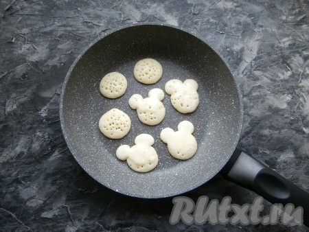 В разогретую сухую сковороду выдавливать из мешка тесто в виде капель диаметром 1-2 см. Если готовите для деток, то сверху оладушка можно выдавить ещё по 2 капли теста в виде ушек. Жарить мини-оладьи на небольшом огне до тех пор, пока на верхней стороне не появятся пузырьки (2-3 минуты).