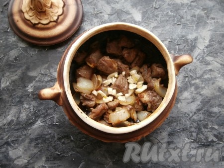 Мясо с луком переложить в горшочек, добавить 2 очищенных и мелко нарезанных зубчика чеснока.
