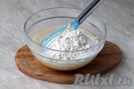 Затем в получившуюся массу постепенно добавляйте, каждый раз хорошо перемешивая венчиком (или ложкой), просеянную муку. Когда замешивать венчиком (или ложкой) станет сложно, продолжайте замешивать дрожжевое тесто руками. Учитывайте, что мука у всех разная, а значит её может понадобиться немного больше или меньше. Ориентируйтесь по консистенции замешиваемого теста.
