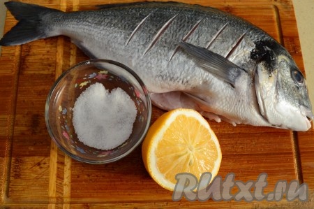 У дорады небольшая чешуя, которая легко удаляется с помощью ножа. Плавники и хвост я не срезала. Разрежьте брюшко и удалите все внутренности, особенно хорошо нужно удалить все чёрные сгустки в районе хребта. Срежьте жабры. С каждой стороны рыбы сделайте острым ножом 4-5 неглубоких разрезов - это позволит запечь рыбку быстрее и более равномерно. Посолите дораду внутри и снаружи (мне на это хватило 2 чайных ложек соли). Переложите рыбку в глубокую посуду. Затем возьмите четверть крупного лимона (или половину среднего) и сбрызните дораду со всех сторон свежевыжатым лимонным соком. Накройте посуду крышкой и отправьте рыбку просолиться и замариноваться в холодильник не менее чем на 30 минут.
