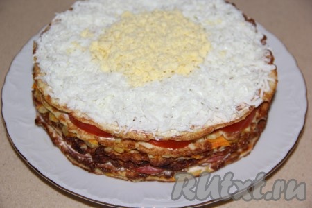 2 яйца заранее отварить в течение 8-10 минут с начала кипения воды, остудить, очистить, а после этого разделить на белки и желтки. Белки натереть на мелкой тёрке и выложить по краю торта. По середине выложить раскрошенный желток, как на фото.
