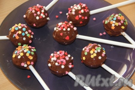 Обмакнуть остывшие кейк-попсы в растопленный шоколад и посыпать цветной посыпкой (пока шоколад не застыл). Чтобы шоколад ровно застыл, пирожные можно поставить в стакан с горохом или гречкой, чтобы они стояли строго вертикально. Стаканы с кейк-попсами можно поставить в холодильник до полного застывания шоколада (для застывания шоколада потребуется буквально пара минут).
