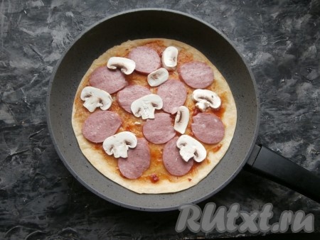 Снять сковороду с огня, смазать лепёшку томатным соусом. Выложить нарезанную кружочками колбасу и нарезанные пластинами шампиньоны.