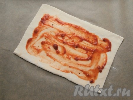 Тесто нужно разделить на 2 одинаковых пласта, немного разморозить и чуточку раскатать на присыпанной мукой поверхности. Один пласт теста смазать томатным соусом (или кетчупом), не доходя до краёв.
