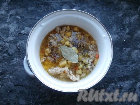 Обжаривать картошку с фаршем, перемешивая, около 3-4 минут на среднем огне. Картофель не должен зажариться, он просто должен соединиться с остальными продуктами. Переложить содержимое сковороды в кастрюлю, влить горячую воду, добавить соль, специи, чёрный молотый перец, лавровый лист. Поставить кастрюлю на сильный огонь, довести до кипения, прикрыть крышкой и варить суп на небольшом огне до готовности картофеля (минут 15).
