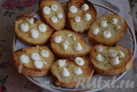 Далее на каждый кусочек чесночной гренки добавляем по 4 капли майонеза. Затем майонез размазываем по всей поверхности гренки.
