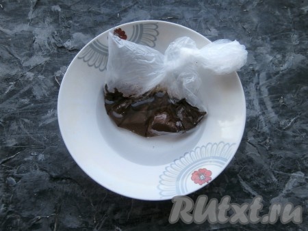 Теперь приготовим крем, для этого нужно поломать шоколад, растопить его на водяной бане, в микроволновке или в целлофановом пакете. Я выложила кусочки шоколада в целлофановый пакет, завязала его, поместила в глубокую тарелку, залила кипятком на несколько минут (шоколад должен полностью растопиться). Растопленный шоколад можно остудить прямо в пакете, а когда понадобится, отрезать кончик у пакета и использовать шоколад.
