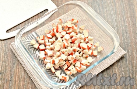 Заранее сварить по отдельности куриное филе и яйца. На варку яиц потребуется минут 8-10 с начала кипения воды. Куриное филе нужно будет отварить в течение минут 25 с момента закипания воды. Отваренные куриное филе и яйца остудить. Разморозить крабовые палочки, затем достать из упаковки и, сняв плёнку, нарезать на мелкие кубики, выложить в достаточно глубокую миску.
