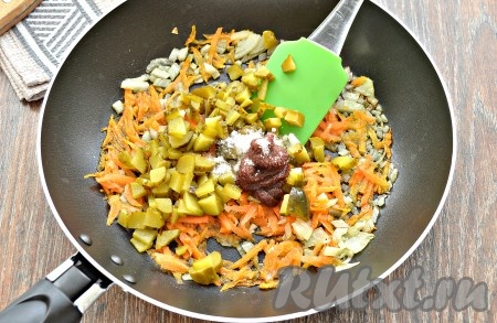 Затем к обжаренным овощам выложить солёный огурец, нарезанный на небольшие кубики, добавить томатную пасту и сахар (сахар поможет уменьшить кислотность), перемешать, обжаривать на сковороде 5 минут, иногда перемешивая, на малом огне.
