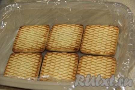 Форму застелить пищевой плёнкой так, чтобы концы плёнки свисали с формы и ширины плёнки хватило завернуть в неё будущее содержимое формы. Выложить на дно формы печенье, как на фото.