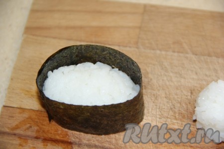 Обернуть рис листом нори (как на фото), край листа смочить и тогда он хорошо прилипнет к другому краю.
