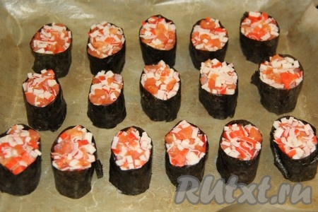 Выложить заготовки роллов на противень, застеленный пергаментом (или тефлоновым ковриком). Поверх риса выложить начинку из рыбы и крабовых палочек.

