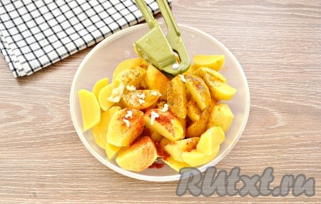 Дольки картофеля посолить, поперчить, приправить специями, добавить очищенные и пропущенные через пресс (или натёртые на мелкой тёрке) зубчики чеснока.
