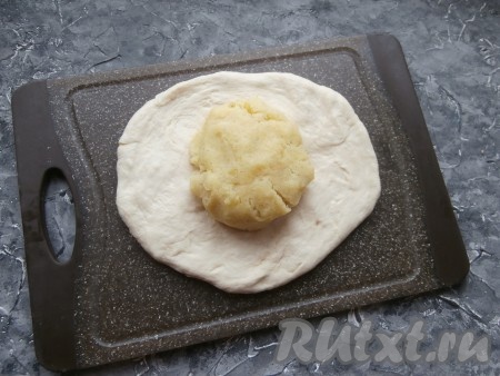 Разделить тесто на 2 части, обмять на столе. Каждую часть теста руками на присыпанной мукой поверхности расплющить в лепёшку толщиной около 1 см. В центр выложить комок картофельной начинки.
