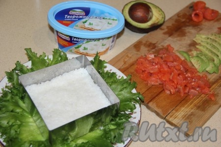 В центр плоской тарелки, покрытой листьями, поставить форму для формирования салата. В форму первым слоем выложить остывший рис и слегка утрамбовать.
