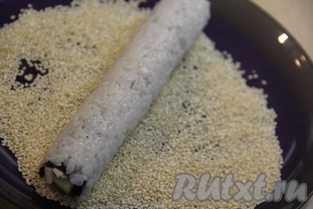 Плотно свернуть ролл с помощью циновки, начиная с края, где отступили 1 см (край без риса). Выложить ролл на плоскую тарелку с кунжутом и обвалять его со всех сторон в кунжуте.
