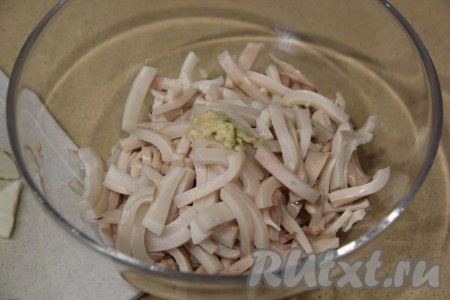 Очищенные зубчики чеснока пропустить через пресс. Добавить чеснок и яйца в салатник к кальмарам.
