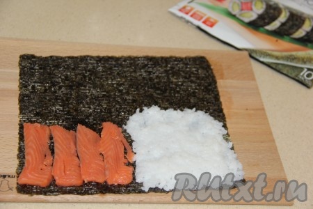 Лист нори обрезать с краю, чтобы получился квадрат. Выложить на доску лист нори и визуально разделить на 4 квадрата. Выложить немного риса на один квадрат и аккуратно распределить. Красную рыбу нарезать тонкими слайсами и выложить после риса на следующий квадрат.
