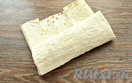 Приступаем к сворачиванию лаваша с начинкой, для этого сначала нужно подогнуть края лаваша по бокам, затем подвернуть край лаваша на начинку. Начиная с подвёрнутого края лаваша с начинкой, нужно свернуть лаваш в форме плоского рулета. 