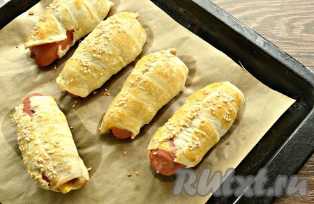 Поставить противень с сосисками с сыром в слоёном тесте в разогретую духовку и выпекать минут 30 при температуре 180 градусов.