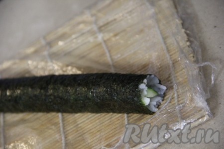 С помощью циновки свернуть ролл, начиная с края, где разместили начинку.