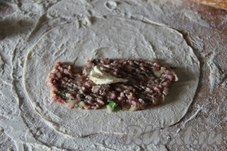 На припылённом мукой столе каждый кусочек теста раскатать скалкой в тонкий круг. На одну часть круга, обступив от краёв, выложить часть мясной начинки. Сверху на фарш положить небольшой кусочек сливочного масла.