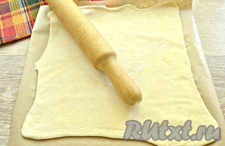 Поверхность стола присыпать мукой. Одну часть слоёного теста раскатать в пласт потоньше. Раскатанное тесто сразу выложить на кулинарный пергамент.