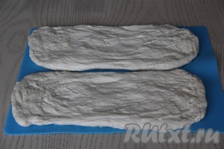 Разделить тесто на 2 части (мы будем готовить 2 французских багета). На силиконовом коврике (или на припылённой мукой поверхности) растянуть руками каждую часть теста в прямоугольник (из 2 частей теста у нас получатся 2 прямоугольника). Накрыть тесто пищевой плёнкой и оставить на 15 минут.