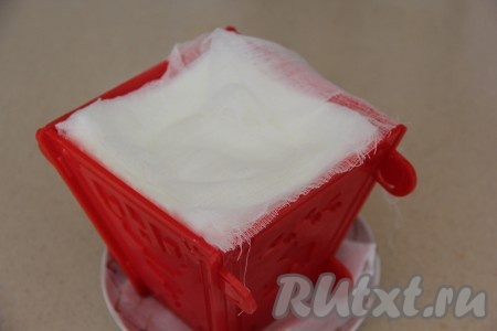 На блюдце выложить бумажное полотенце, сложенное в несколько слоёв (или салфетку), сверху поставить форму с творожно-кокосовой массой. На блюдце, на котором стоит форма, будет сливаться жидкость, выделяющаяся из творожно-кокосовой массы. Поверх марли, покрывающей верх формы, поставить блюдце и груз (в качестве груза можно использовать, например, банку с водой). Форму вместе с грузом часов на 10-12 поставить в холодильник. Я периодически меняю бумажное полотенце, на котором стоит форма с пасхой, на сухое. 