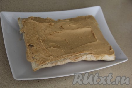 Выложить первый корж на тарелку и смазать частью крема.