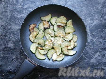 Поместить полукружочки цукини в сковороду с разогретым растительным маслом, на достаточно сильном огне обжарить их, помешивая, до золотистости (около 5-6 минут). Добавить измельчённый чеснок, соль и перец чёрный молотый по вкусу.