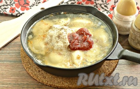 Как только вода в сковороде с пельменями и луком закипит, добавляем к ним сметану и томатный соус, по вкусу солим и перчим.