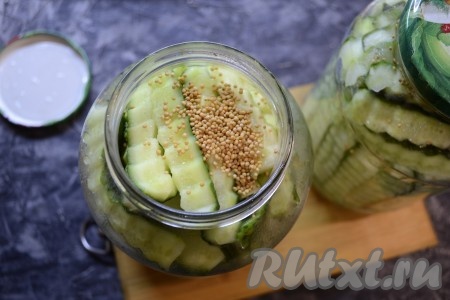 Далее воду из банок с огурчиками слить в кастрюлю, вскипятить и снова залить огурцы в банке, оставив их под прикрытой крышкой на 5 минут. Затем воду из баночек слить в кастрюлю, в каждую банку с огурцами всыпать по 1 чайной ложке сухой зерновой горчицы.