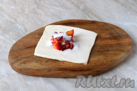 Одну часть слоёного теста немного раскатать скалкой (или размять пальцами), чтобы тесто стало тоньше и получился квадрат. В центр квадрата выложить, примерно, 1 столовую ложку сливовой начинки и чайную ложечку сахара. В зависимости от сладости слив, сахара можно добавить немного меньше или больше. 