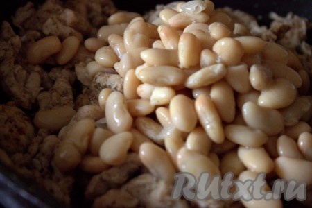 Затем с консервированной фасоли слить жидкость, добавить её в сковороду с обжаренными кусочками куриного мяса и перемешать.