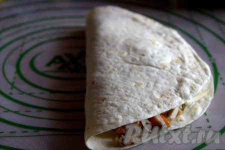 Чистым краем тортильи накрыть край с начинкой, складывая тортилью пополам, затем слегка прижать рукой.